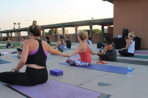 three women holding hands during a yoga class outdoors, seated on yoga mats.